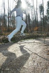 Frau springt beim Waldlauf ueber ein Hindernis