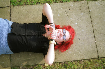 Junge Frau mit roten Haaren liegt lachend in der Sonne