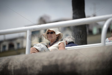 Nizza  Frankreich  eine aeltere Frau sitzt an der Promenade des Anglais