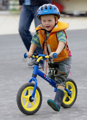 Kleiner Junge mit Schutzhelm auf Laufrad