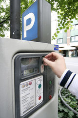 Mann wirft Muenzgeld in einen Parkscheinautomat