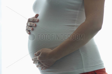 Schwangere Frau haelt schuetzend ihre Haende vor den Bauch