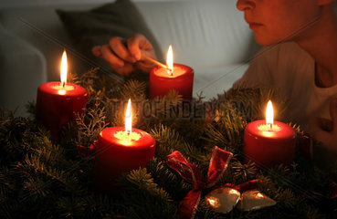 Frau zuendet die vierte Kerze am Adventskranz an