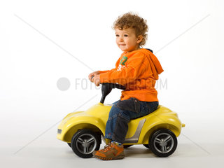 Kleiner Junge auf einem gelben Spielzeugauto