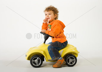 Kleiner Junge auf einem gelben Spielzeugauto