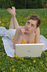 Frau mit ihrem Laptop auf einer Blumenwiese