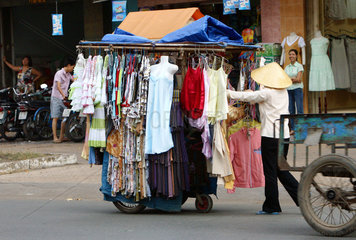Eine Frau schiebt einen Strassen-Verkaufsstand mit Bekleidung in den Strassen Saigons