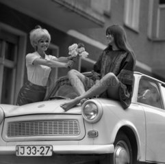 Berlin  DDR  Modeaufnahme  Modefotografie  junge Frau reicht ihrer auf einem Trabant sitzenden Freundin Blumen