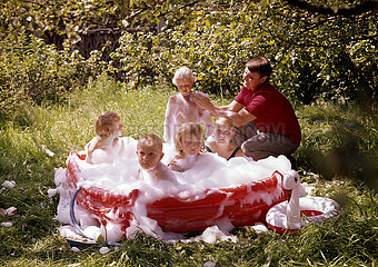 Strausberg  Deutsche Demokratische Republik  Vater seift seine Kinder im Garten in einem Planschbecken ein
