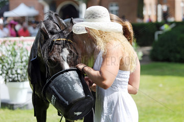 Hoppegarten  Frau mit Hut laesst ein Pferd Wasser aus einem Eimer saufen