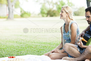 Woman listening to man playing acoustic guitar while picnicking in park