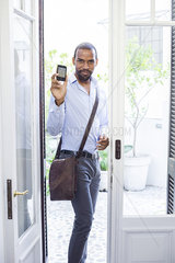 Man standing in open doorway  showing smartphone and smiling
