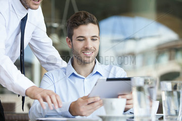 Businessman showing colleague how to use digital tablet