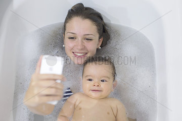 Mother using smartphone to photograph herself and baby while taking a bath