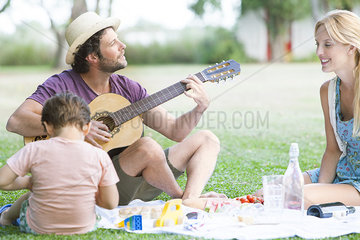 Man playing acoustic guitar next to wife and son
