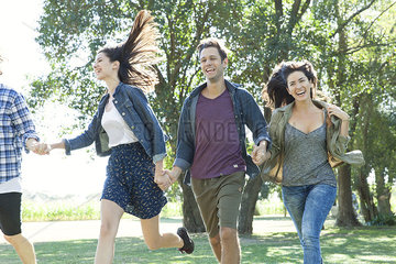 Friends holding hands running carefree through a park