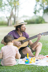 Father playing acoustic guitar next to son