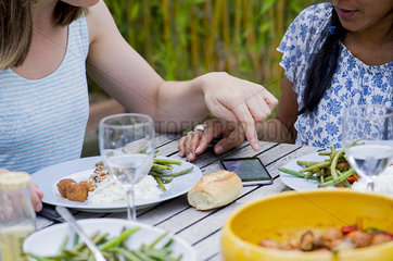 Women looking at smartphone while dining together outdoors