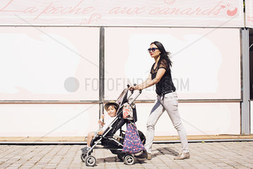 Mother pushing toddler son in stroller on sidewalk