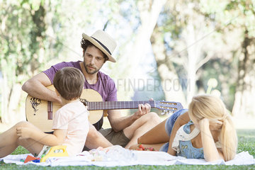 Man playing acoustic guitar for wife and son