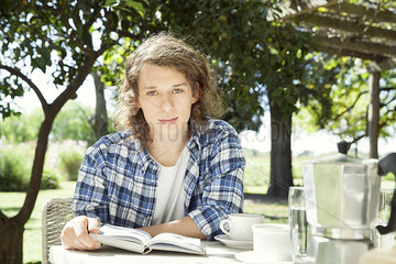 Young man sitting at breakfast table outdoors with book