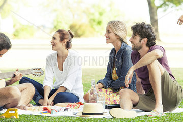 Firends listening to man playing guitar while picnicking in park