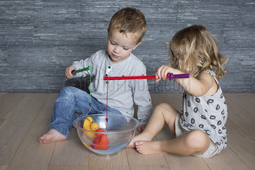Children using toy fishing rods to catch rubber ducks floating in large bowl