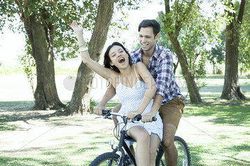 Young couple riding bicycle together with girlfriend seated sidesaddle on crossbar