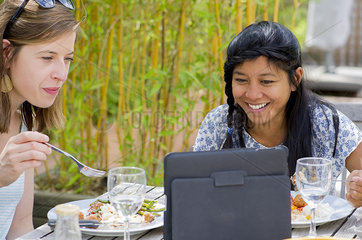 Women watching digital tablet while eating outdoors