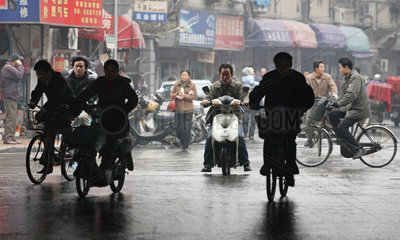 Shanghai  Fahrradfahrer und Motorradfahrer auf regennasser Strasse