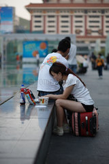 Shenzhen  China  junge Frau sitzt auf ihrem Koffer und arbeitet an ihrem Laptop