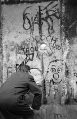 Berlin  Deutschland  Mann schaut durch ein Loch in der Mauer auf den Grenzstreifen