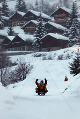 Belalp  Schweiz  Menschen rodeln einen Hang hinunter  im Hintergrund stehen Ferienhaeuser