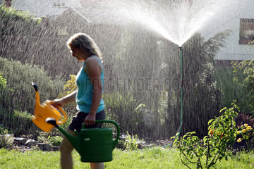 Cottbus  Deutschland  Frau mit Giesskannen vor einem Gartensprenger