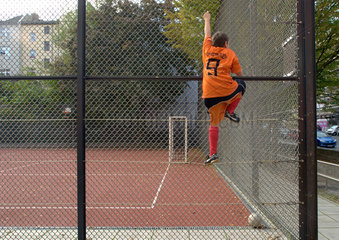 Berlin  Deutschland  Junge im Oranje-T-Shirt klettert ueber Zaun