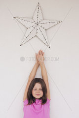 Girl reaching toward star shape hanging above her head  eyes closed