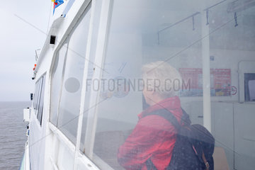 Deutschland  eine Frau schaut durch die Fenster einer Faehre auf die Nordsee
