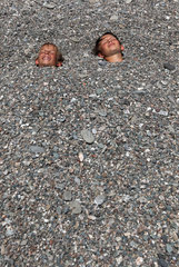 Fiumefreddo  Italien  Jungen sind vollstaendig mit Kieselsteinen bedeckt