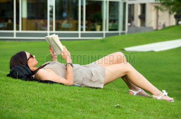 Hamburg  Deutschland  junge Frau liegt im Sandtorpark auf der Wiese und liest ein Buch