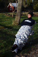Lessebo  Schweden  Frau ruht sich in eine Decke gehuellt im Garten aus