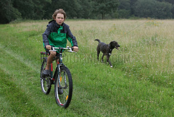 Neu Kaetwin  Deutschland  Junge faehrt Fahrrad neben einem Hund auf einer Wiese