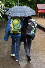 Berlin  Deutschland  Jugendliche laufen bei Regenwetter zusammen unter einem Regenschirm