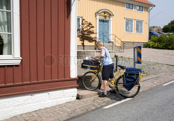 Fjaellbacka  Schweden  eine Postbotin traegt mit dem Fahrrad die Post aus