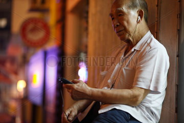 Hongkong  China  ein alter Mann sitzt in den Strassen von Hong Kong und hoert Musik