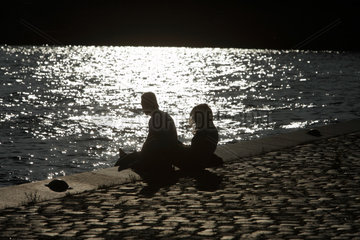 Berlin  Deutschland  zwei Menschen sitzen in der Abendsonne am Ufer der Spree