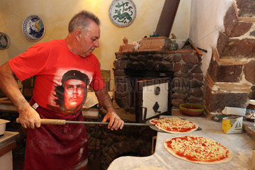 Torre Alfina  Italien  Pizzabaecker schiebt eine Pizza auf einen Backschieber