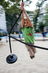 Berlin  Deutschland  Junge haengt an einer Seilbahn auf einem Kinderspielplatz