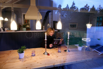 Blavand  Daenemark  junge Frau liest abends eine Zeitschrift in einem Ferienhaus