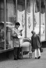 Berlin  Deutsche Demokratische Republik  Maedchen schaut in den Kinderwagen eines Zeitung lesenden Mannes
