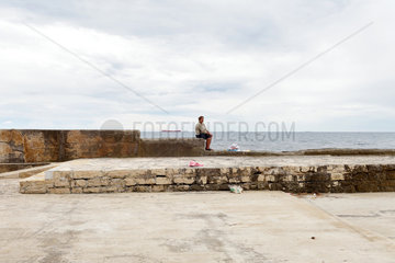 Novigrad  Kroatien  eine Frau sitzt auf der Hafenmauer an der Strandpromenade